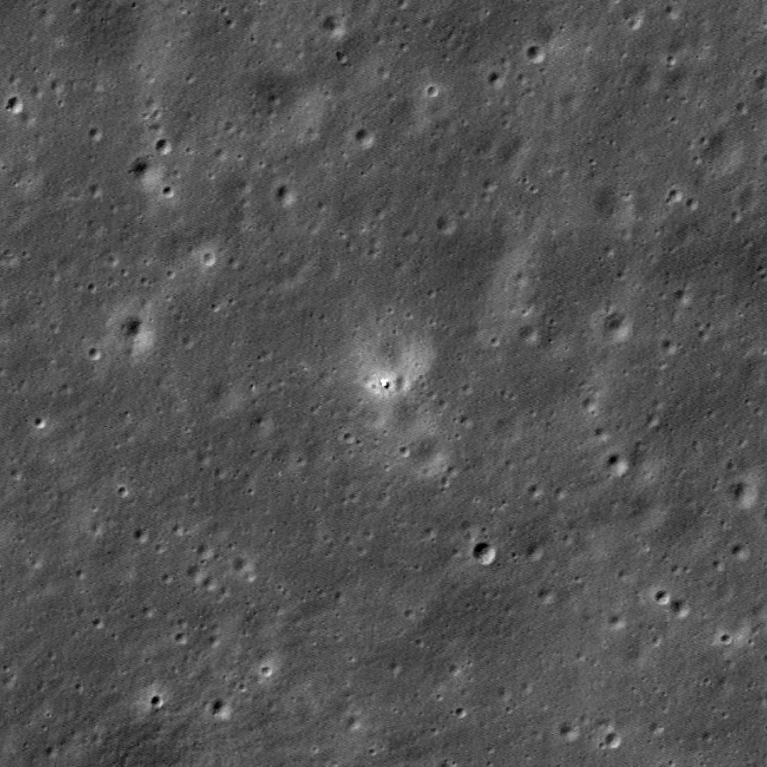 Suelo lunar gris salpicado de cráteres pequeños, con un punto brillante rodeado de un halo claro en el centro.