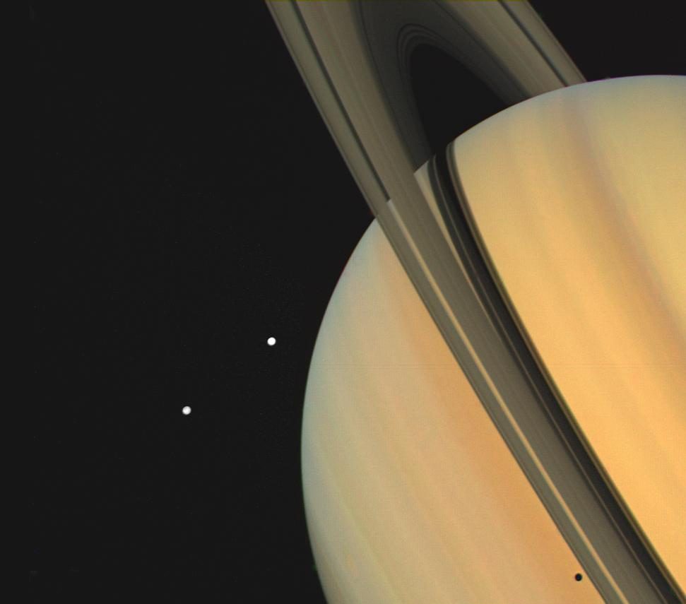 Saturno visto de cerca, cortado por el borde derecho de la imagen, con los anillos en diagonal y dos lunas pequeñas cerca del planeta.