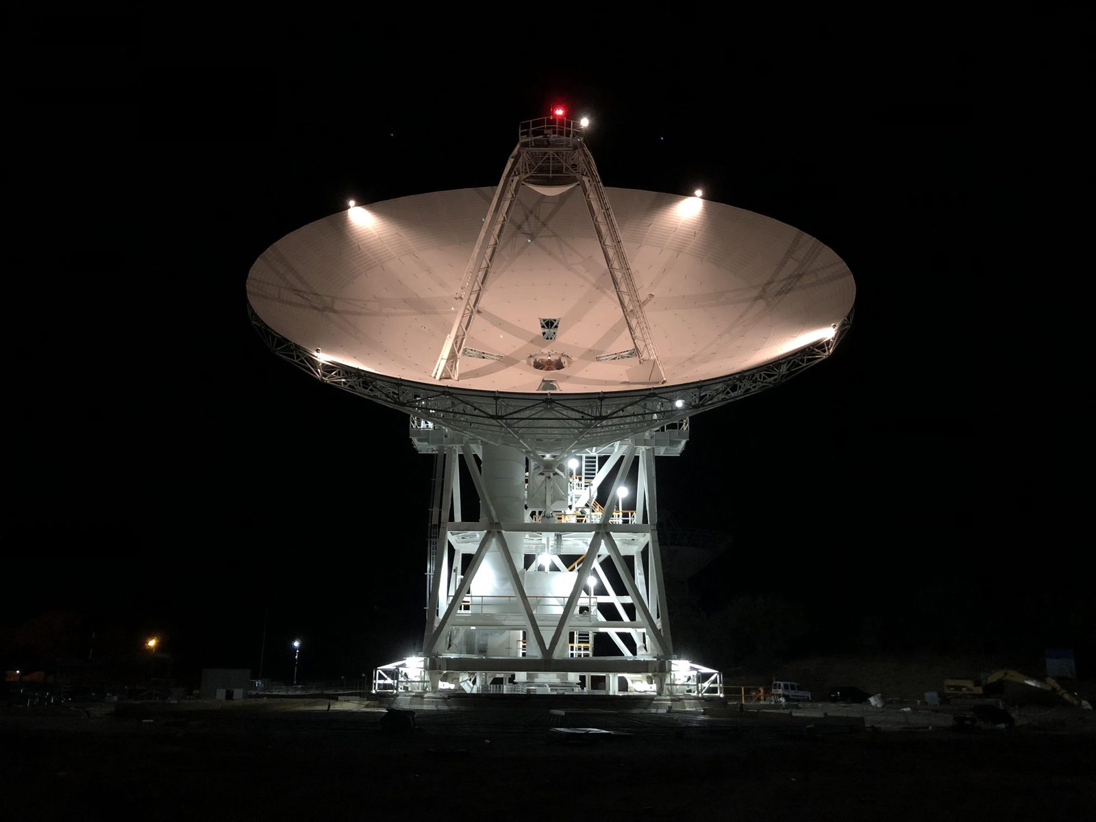 Una antena parabólica iluminada de noche, con el plato apuntando al cielo oscuro.