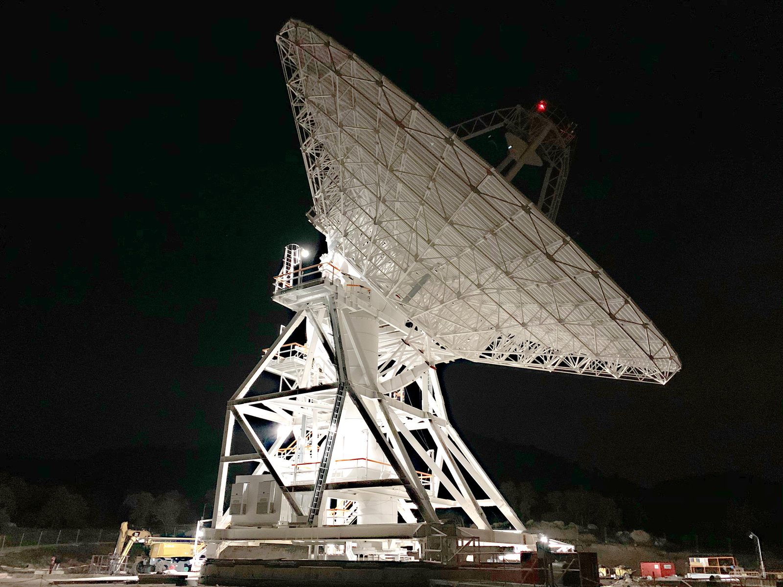Una antena parabólica iluminada desde abajo en la noche, con otra antena en sombra detrás.
