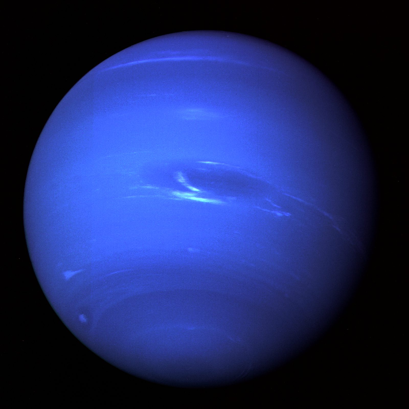 Disco azul de Neptuno sobre fondo negro, con una mancha oscura alargada en el hemisferio sur y algunas nubes blancas brillantes.