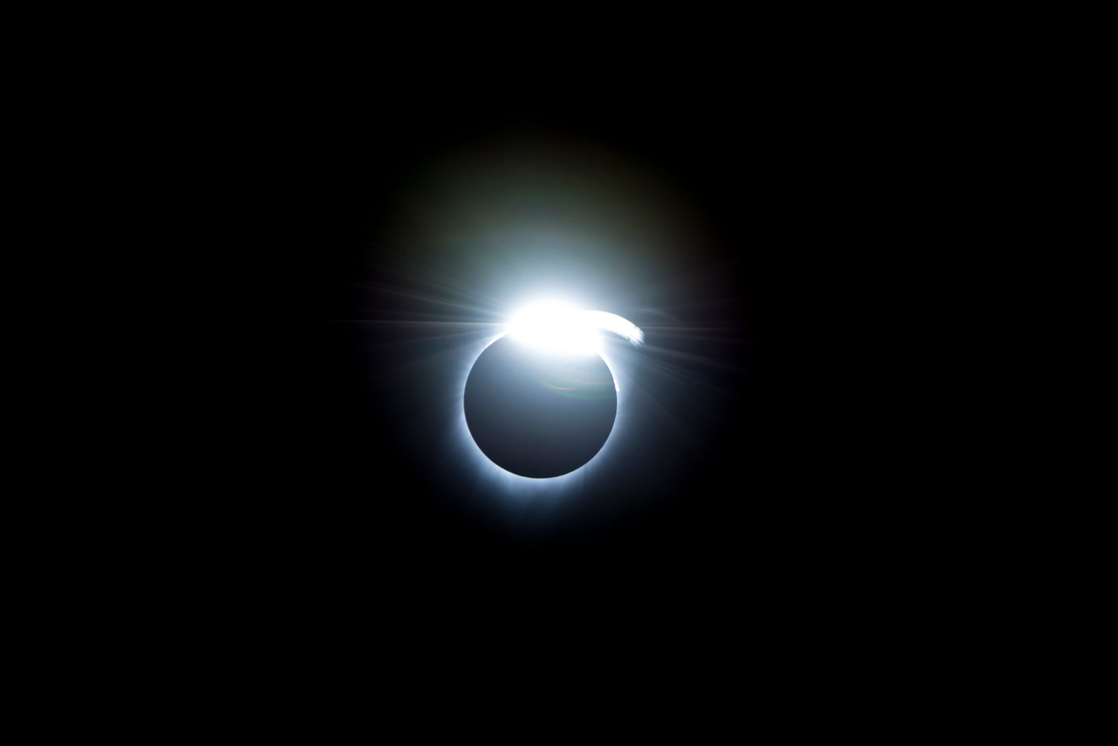 Un anillo delgado de luz alrededor del disco negro de la Luna con un punto muy brillante en un costado, como un diamante engarzado.