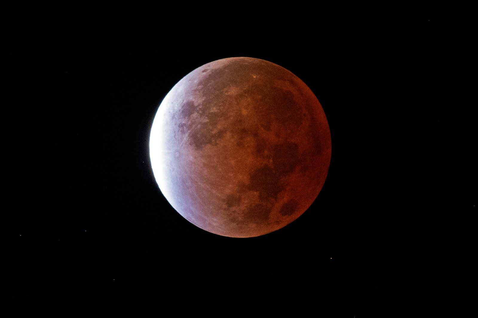 La Luna con la mayor parte del disco teñida de rojo cobrizo y una franja blanca brillante en el borde superior.