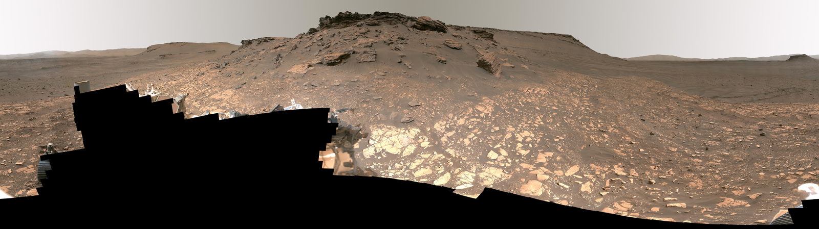 Panorama de la superficie de Marte: terreno rocoso ocre en primer plano y, al fondo, los escarpes de un antiguo delta.